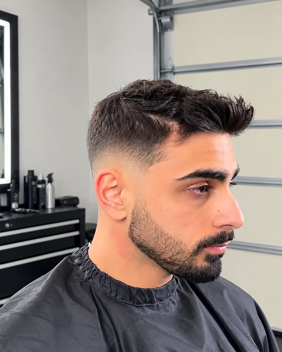 Textured top with a low skin fade and trimmed beard, side profile