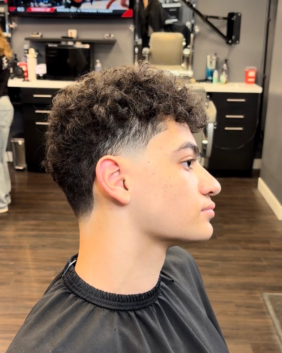 Natural curly top with a low taper fade, side profile